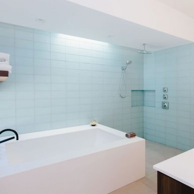 Ranch Redux - Interior view of the modern, light-filled master bathroom. A narrow skylight illuminates the light blue glass tile along the shower and soaking tub. Photograph by Tomoko Matsubayashi.