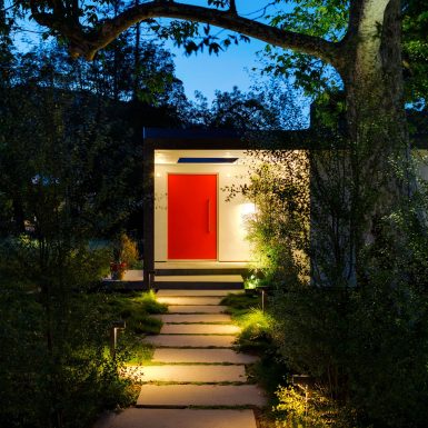 Ranch Redux - Exterior view of red front door at dusk, with landscape and modern paver walkway lit with warm pathway lighting in the foreground. Photograph by Trevor Tondro.