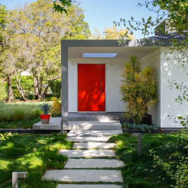 Ranch Redux - Exterior view of red front door and skylight. Modern concrete paver pathway and grassy landscape in the foreground. Photograph by Trevor Tondro.